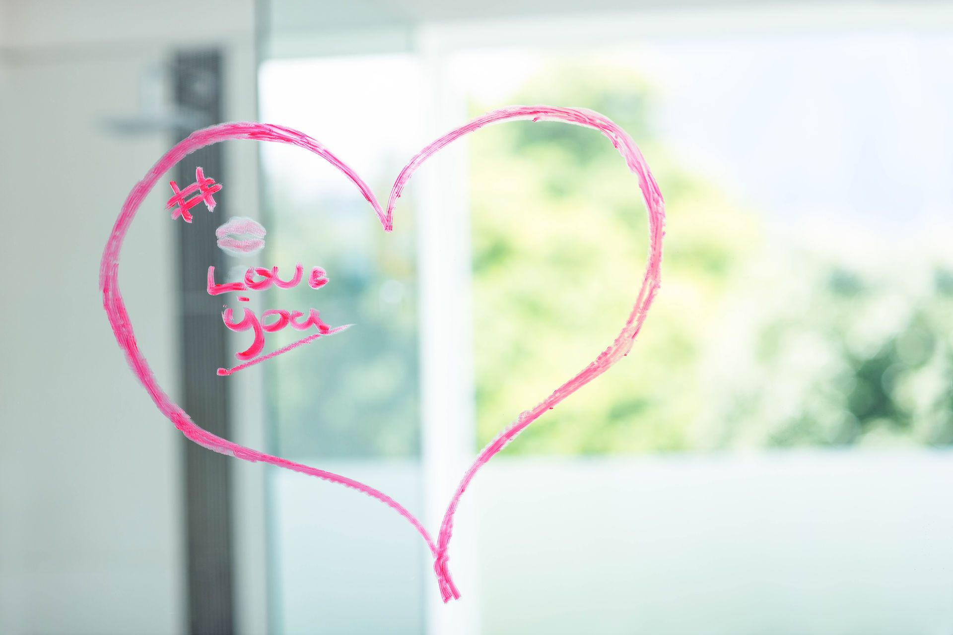 The words "love you" inside a love heart written in pink lipstick on a mirror The words "love you" inside a love heart written in pink lipstick on a mirror